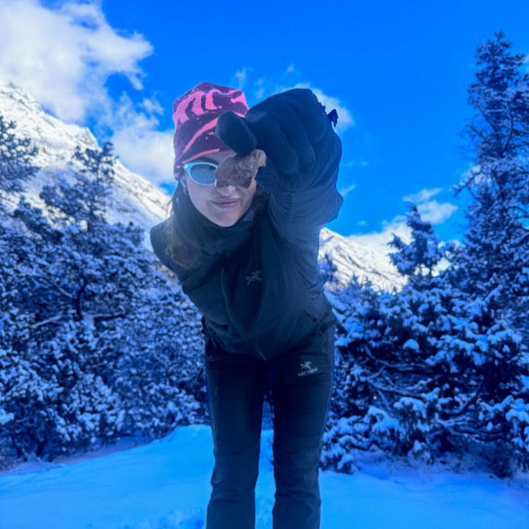 Person in winter clothing with a snowy landscape and blue sky with campers pantry choc freeze dried ice cream